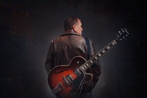 Image DC Scott wearing leather jacket with electric guitar on back